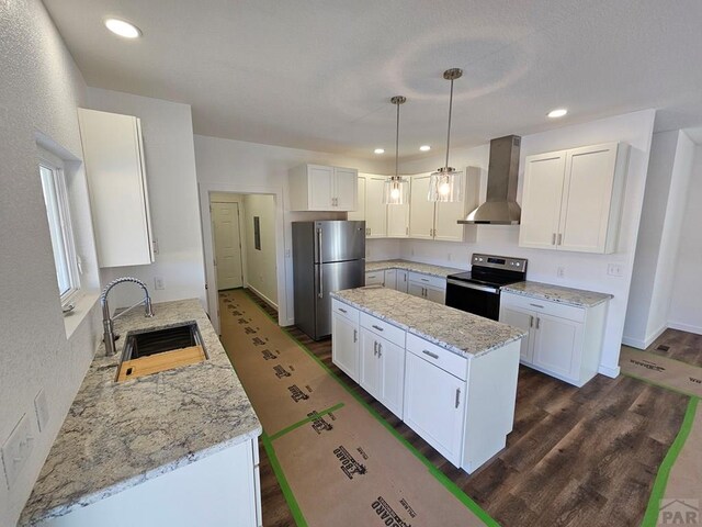 kitchen with white cabinets, appliances with stainless steel finishes, decorative light fixtures, wall chimney range hood, and a sink