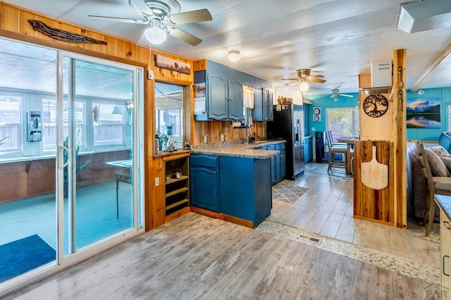 kitchen with blue cabinets, wood walls, light wood finished floors, and stainless steel fridge with ice dispenser