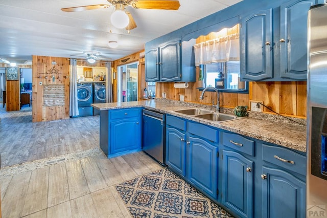 kitchen with wooden walls, washer and clothes dryer, appliances with stainless steel finishes, blue cabinets, and a sink