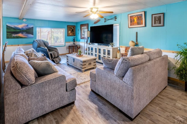 living area with baseboards, beam ceiling, a ceiling fan, and wood finished floors