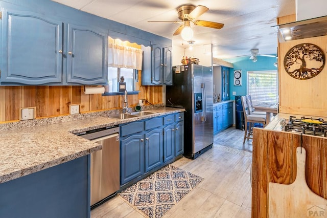 kitchen with extractor fan, wooden walls, blue cabinets, a sink, and appliances with stainless steel finishes