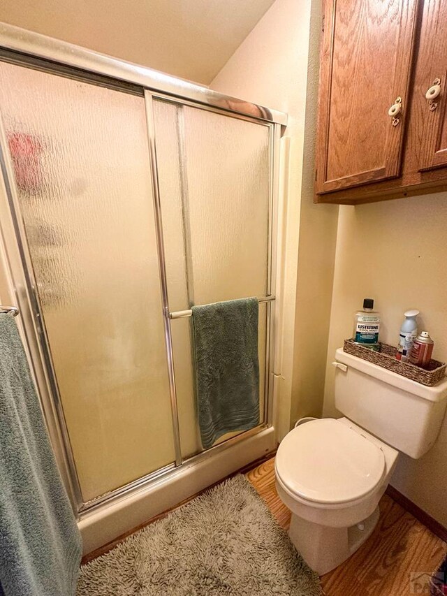 bathroom featuring toilet, baseboards, wood finished floors, and a shower with shower door