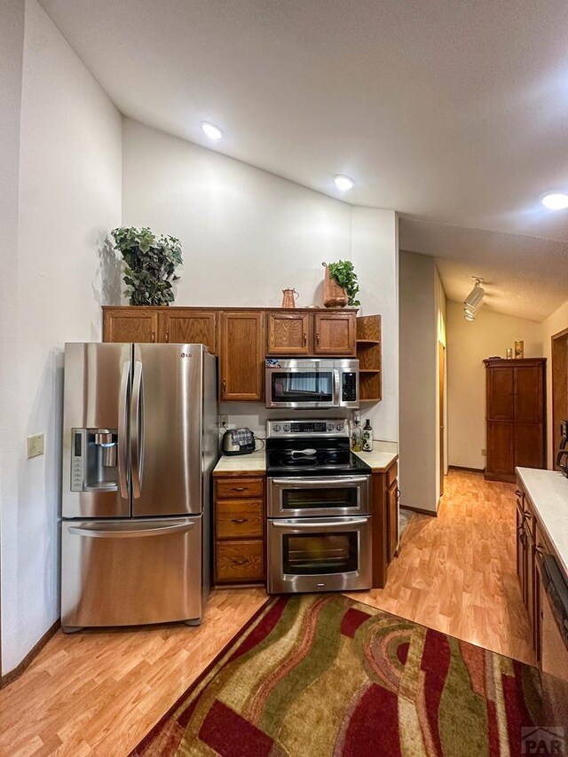 kitchen featuring light wood-style flooring, stainless steel appliances, baseboards, light countertops, and brown cabinets