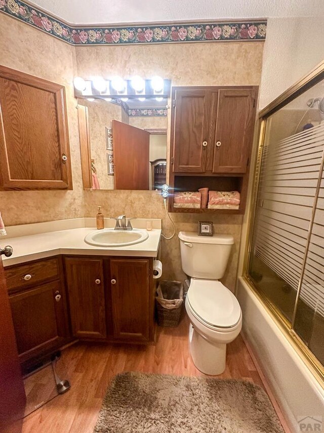 full bath with bath / shower combo with glass door, vanity, toilet, and wood finished floors