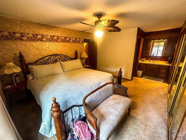 bedroom featuring a textured ceiling, connected bathroom, light carpet, a sink, and a ceiling fan