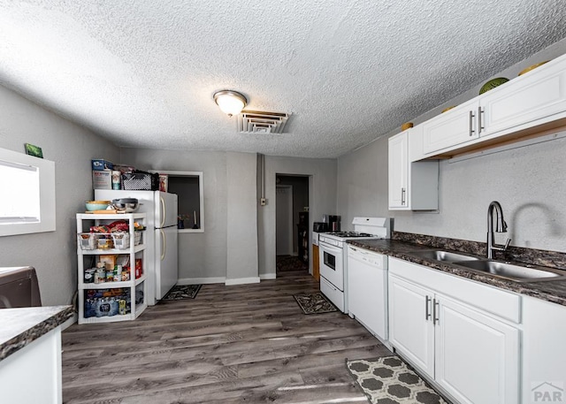 kitchen with white appliances, dark wood-type flooring, a sink, white cabinets, and dark countertops