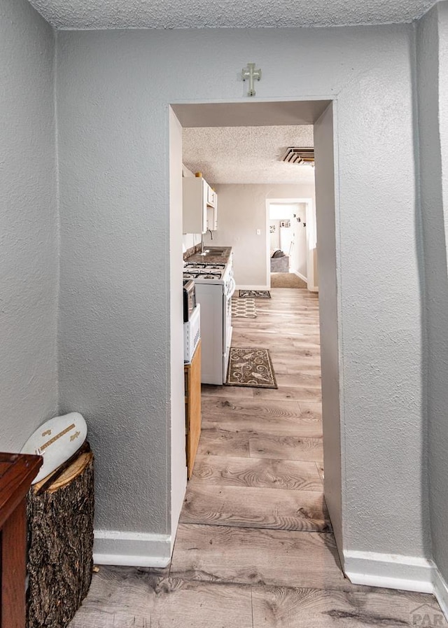 corridor with light wood-style flooring, baseboards, a textured ceiling, and a textured wall