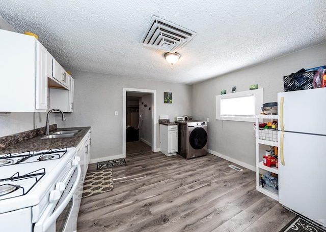 kitchen featuring white appliances, wood finished floors, a sink, white cabinetry, and washer / clothes dryer