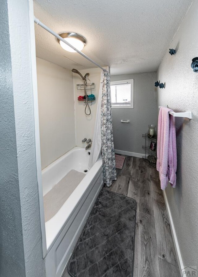 full bathroom with a textured ceiling, a textured wall, wood finished floors, and shower / bathtub combination with curtain