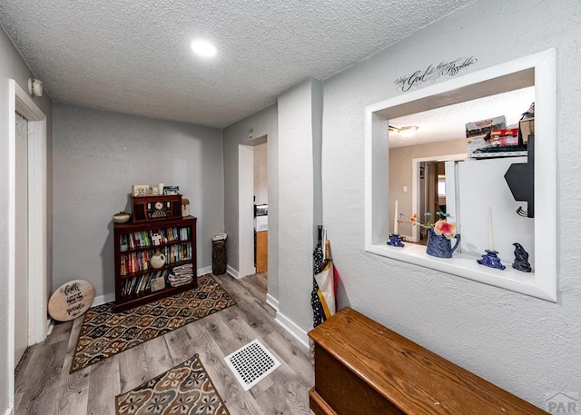 hall featuring light wood finished floors, baseboards, visible vents, and a textured ceiling