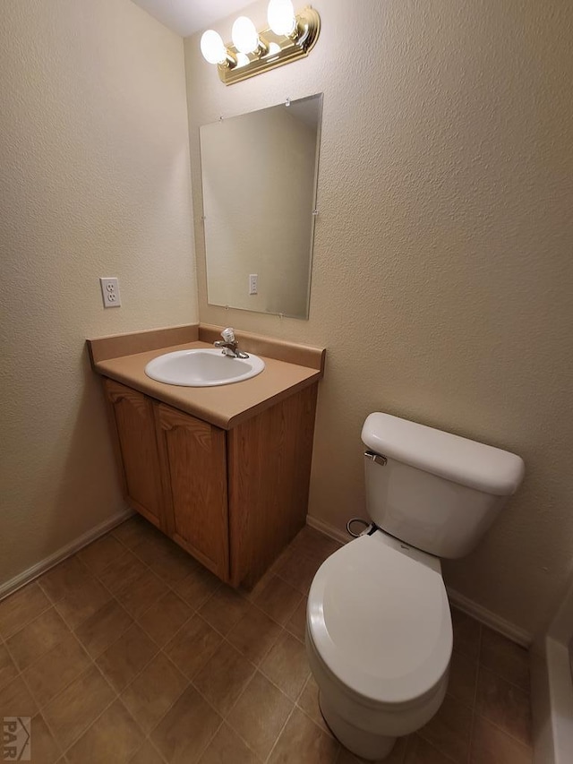 half bathroom featuring baseboards, a textured wall, toilet, tile patterned flooring, and vanity