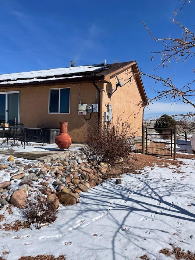 snow covered property featuring roof mounted solar panels, fence, a patio, and stucco siding