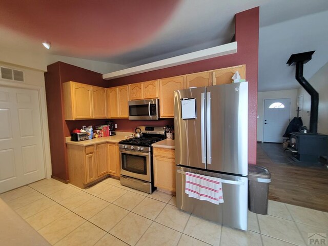 kitchen with stainless steel appliances, light countertops, visible vents, light brown cabinetry, and a wood stove