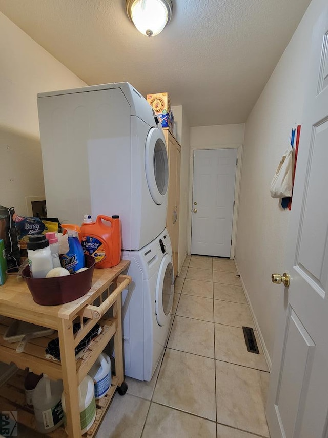 clothes washing area with stacked washer and clothes dryer, visible vents, light tile patterned flooring, a textured ceiling, and laundry area