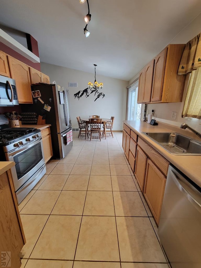 kitchen with light tile patterned floors, stainless steel appliances, light countertops, hanging light fixtures, and a sink