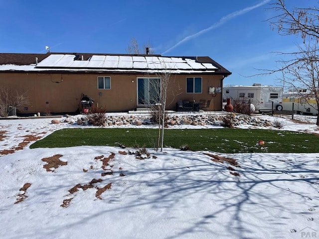 snow covered rear of property with stucco siding and solar panels