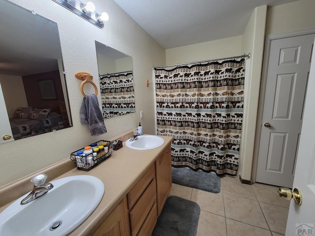 full bathroom featuring a textured wall, tile patterned flooring, a sink, and double vanity