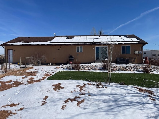 snow covered back of property with roof mounted solar panels and stucco siding