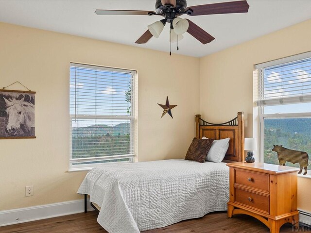 bedroom with a ceiling fan, wood finished floors, baseboards, and baseboard heating