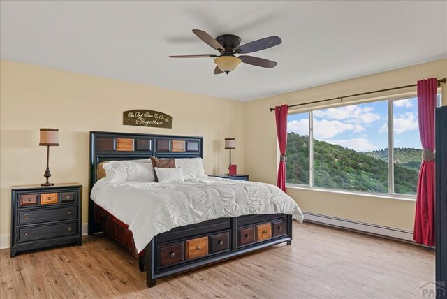 bedroom with a baseboard heating unit, wood finished floors, and a ceiling fan