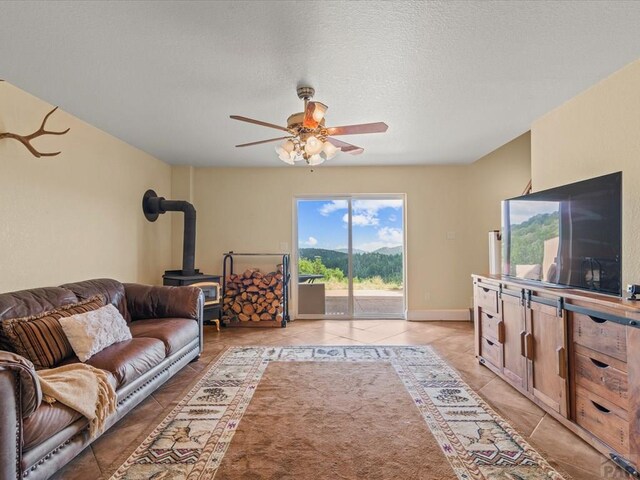 living area with a ceiling fan, a textured ceiling, light tile patterned flooring, and a wood stove