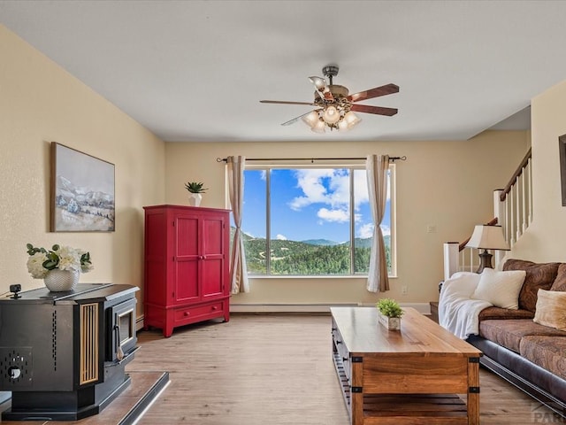 living area with stairway, light wood-style flooring, a wood stove, and a baseboard radiator