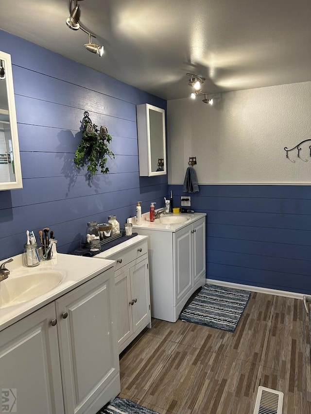 25433 County Rd 25, La Junta, CO 81050 - bathroom with rail lighting, wood finished floors, wooden walls, two vanities, and a wainscoted wall