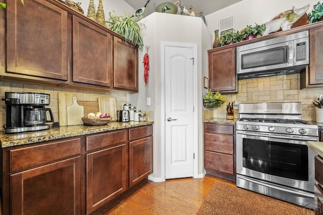 kitchen featuring decorative backsplash, appliances with stainless steel finishes, light stone countertops, and light wood finished floors