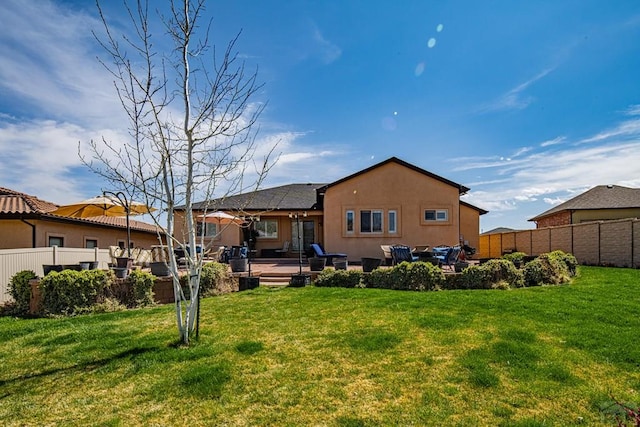 rear view of house featuring a yard, stucco siding, and fence