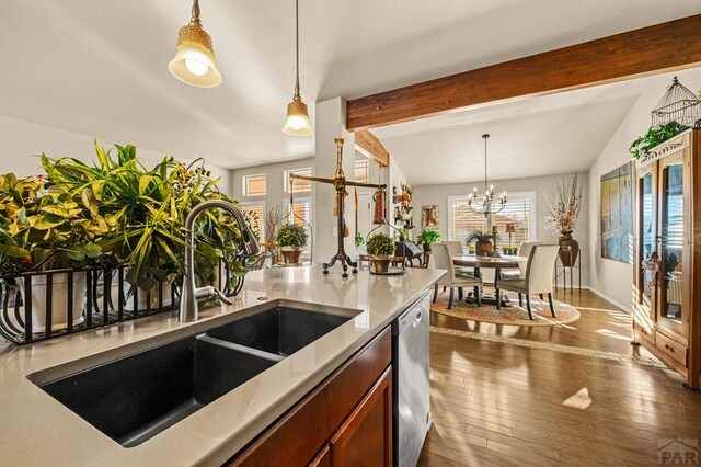 kitchen with decorative light fixtures, beamed ceiling, dark wood finished floors, stainless steel dishwasher, and a sink