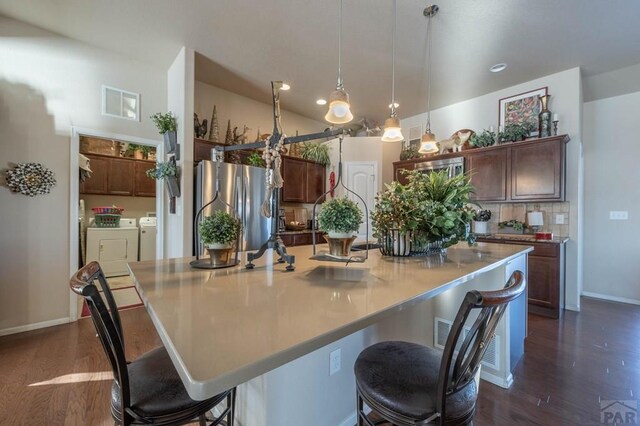 kitchen with hanging light fixtures, washer and dryer, freestanding refrigerator, a spacious island, and dark wood-type flooring