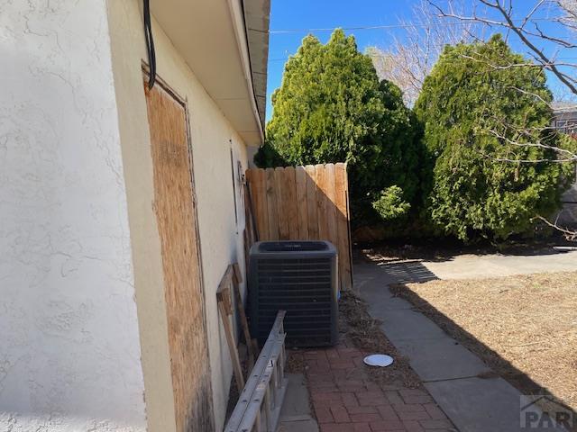 view of property exterior with central AC, stucco siding, and fence