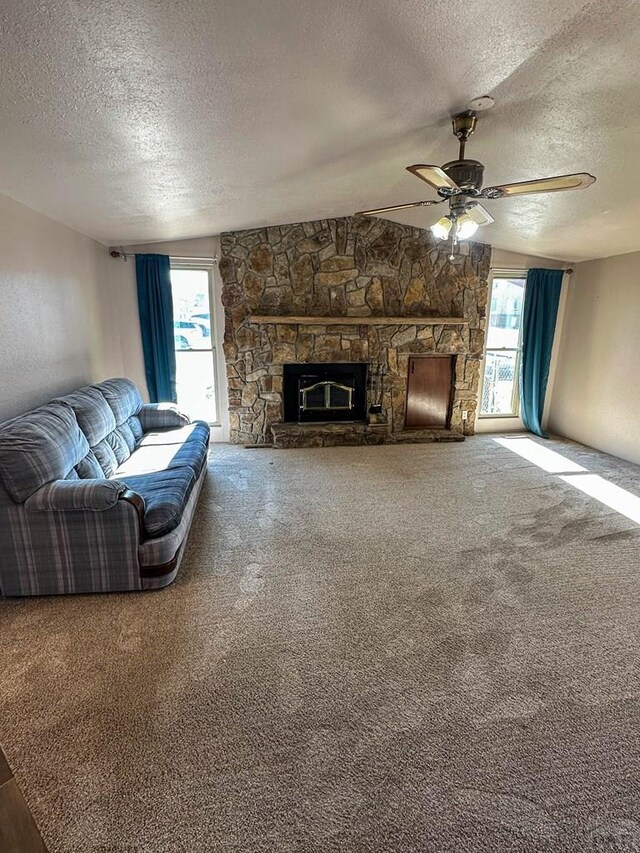 carpeted living area with a textured ceiling, a stone fireplace, and a healthy amount of sunlight