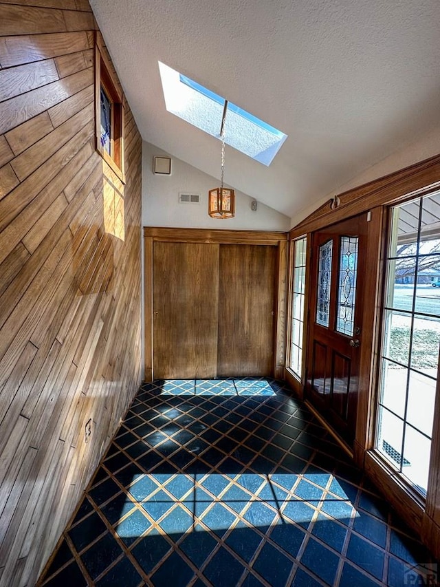 foyer entrance featuring lofted ceiling with skylight, visible vents, wood walls, and a textured ceiling