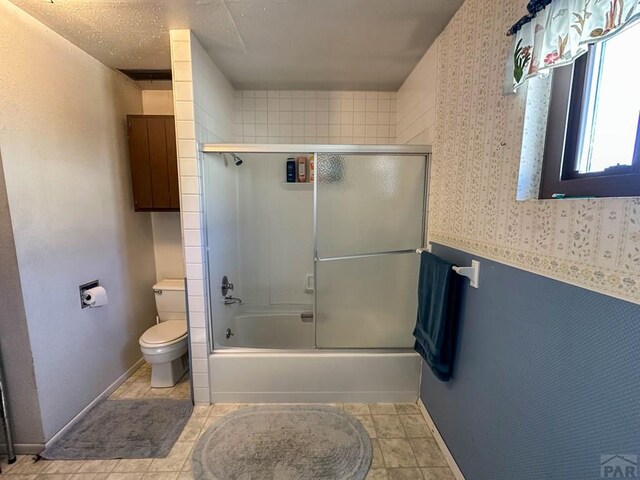 bathroom featuring baseboards, shower / bath combination with glass door, toilet, and tile patterned floors