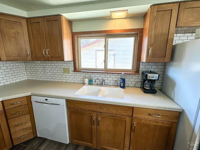 kitchen with tasteful backsplash, dishwasher, brown cabinets, light countertops, and a sink