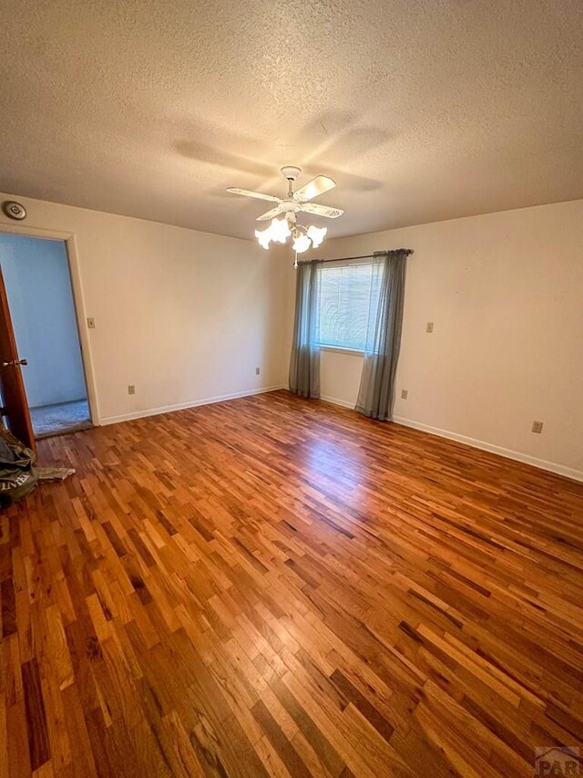 empty room with ceiling fan, a textured ceiling, baseboards, and wood finished floors