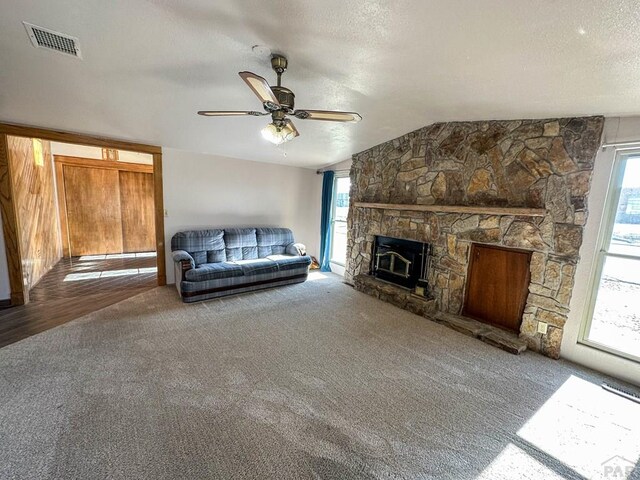 living area featuring visible vents, plenty of natural light, a stone fireplace, and a textured ceiling