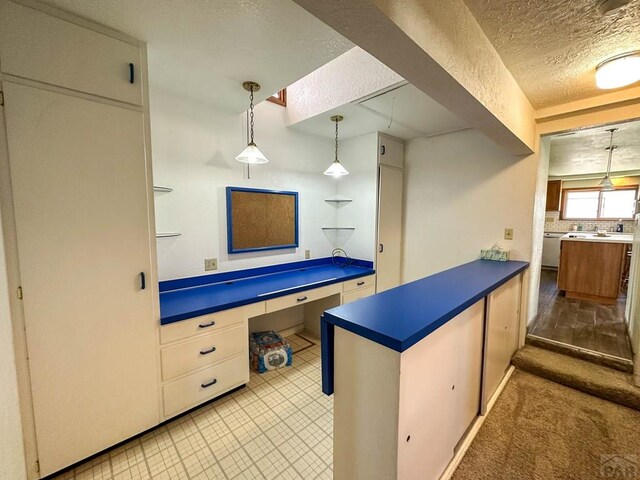 kitchen featuring built in desk, open shelves, dark countertops, hanging light fixtures, and a textured ceiling