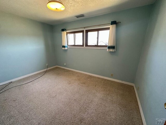 empty room with carpet floors, visible vents, a textured ceiling, and baseboards