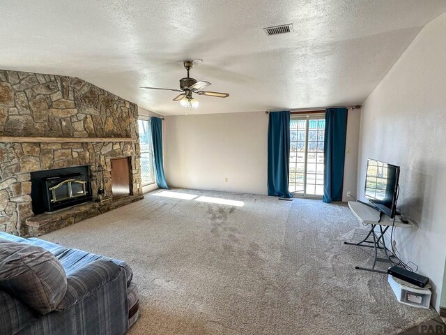 living room featuring carpet floors, visible vents, vaulted ceiling, a stone fireplace, and a textured ceiling