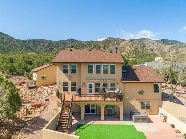 back of property with roof with shingles, stucco siding, a deck with mountain view, stairway, and a patio area