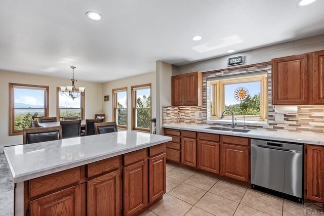 kitchen with pendant lighting, light countertops, brown cabinetry, a sink, and dishwasher