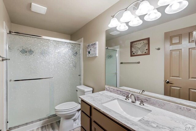 full bath featuring a stall shower, vanity, toilet, and wood finished floors