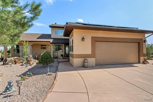 view of front of property with a garage, solar panels, driveway, and stucco siding