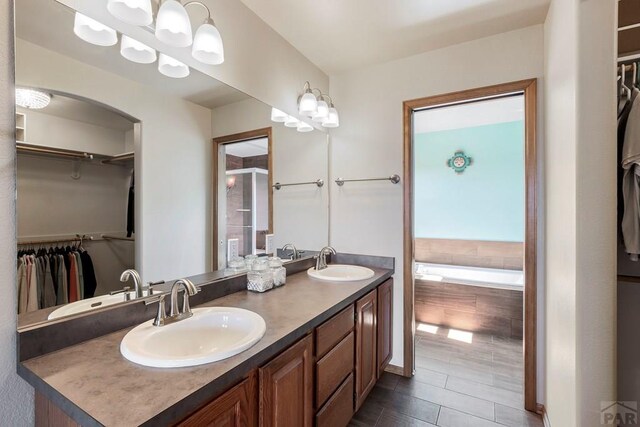 bathroom with double vanity, a garden tub, a walk in closet, and a sink