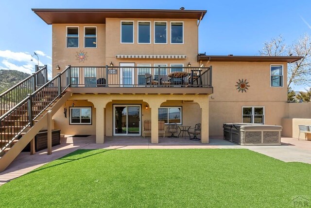 back of property with a patio, stucco siding, a lawn, a hot tub, and stairway