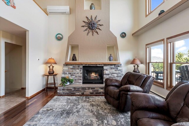 living area featuring dark wood-style floors, a wall mounted AC, a baseboard heating unit, a glass covered fireplace, and baseboards