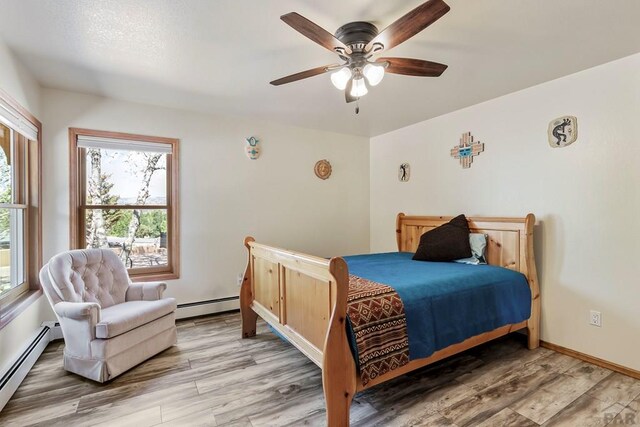 bedroom with a baseboard heating unit, wood finished floors, and baseboards