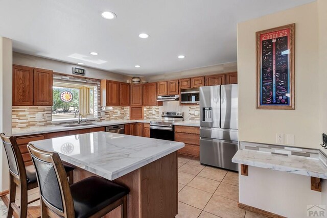 kitchen featuring appliances with stainless steel finishes, a sink, a center island, and a kitchen breakfast bar